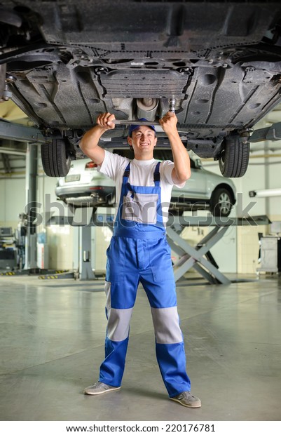 Car mechanic examining car suspension of\
lifted automobile at repair service\
station