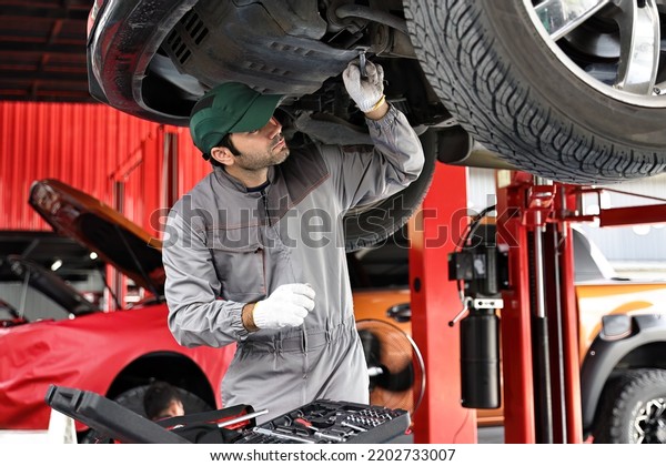 Car mechanic examining car suspension\
of lifted automobile at repair service station.\
