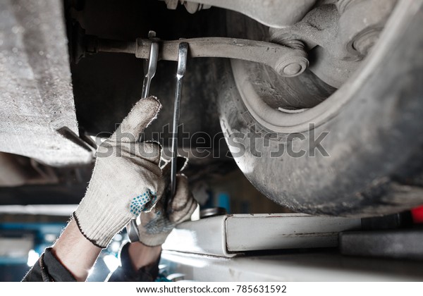car mechanic examining car suspension of\
lifted automobile at repair service\
station