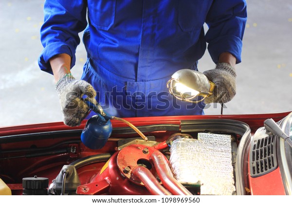Car mechanic examining car using flashlight\
checking oil in auto repair\
service.