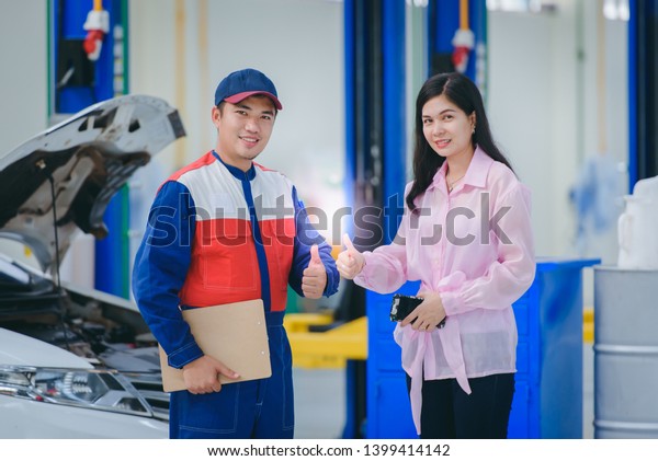 A car mechanic and a female\
customer smiling and raising a happy hand in a car repair shop, a\
beautiful Asian woman customer is happy in the service of a\
repairman.