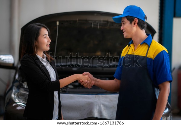 The\
car mechanic and the female customer talk and hold hands to repair\
the car of the girl in the car repair shop, holding hands to agree\
and the customers are happy to service the\
repairman.