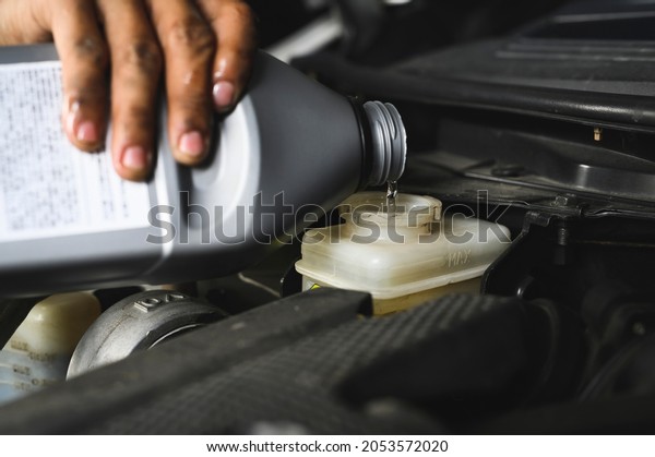 Car mechanic filling brake fluid in brake\
fluid reservoir.