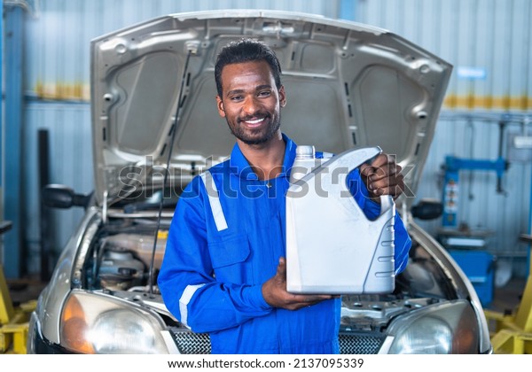 Car mechanic at garage with Oil container in hand\
looking at camera - concept of car maintenance, lubrication and\
repair service