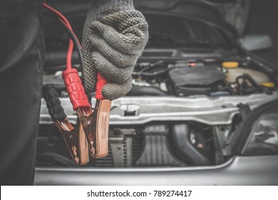 Car mechanic hands in gloves is ready charging a discharged battery with booster jumper cables in the garage. Problems and solutions concept. Cares about automobile.