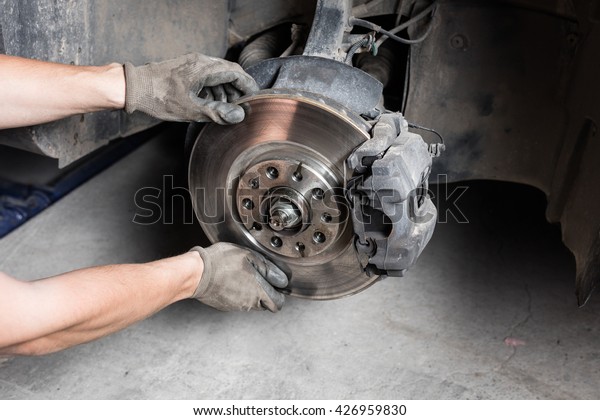 Car mechanic hands\
replace brakes in garage. Mechanic technician worker installing car\
wheel at maintenance.  Worker changing brake disc. Brake disc\
installation concept.
