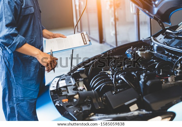 Car mechanic holding clipboard and checking to\
maintenance vehicle by customer claim order in auto repair shop\
garage. Engine repair service. People occupation and business job.\
Automobile technician