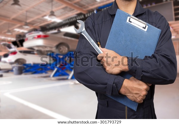 Car mechanic holding a\
clipboard of service order with wrench for maintaining car at the\
repair shop