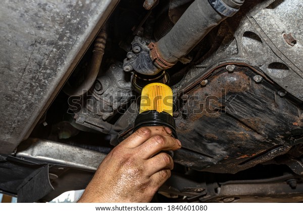 Car mechanic holding\
a new oil filter for a diesel engine in the background oil pan from\
the engine.