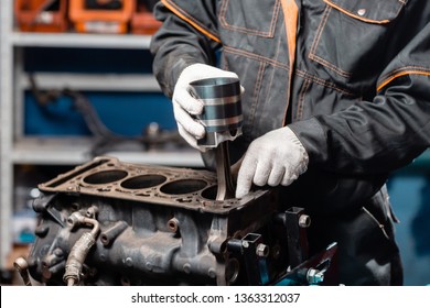 Car mechanic holding a new piston for the engine, overhaul.. Engine on a repair stand with piston and connecting rod of automotive technology. Interior of a car repair shop.
