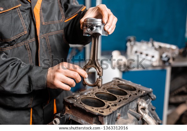 Car mechanic\
holding a new piston for the engine, overhaul.. Engine on a repair\
stand with piston and connecting rod of automotive technology.\
Interior of a car repair\
shop.