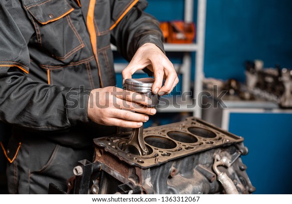 Car mechanic\
holding a new piston for the engine, overhaul.. Engine on a repair\
stand with piston and connecting rod of automotive technology.\
Interior of a car repair\
shop.