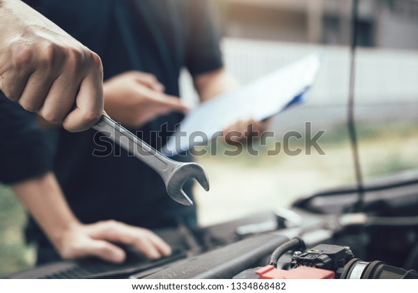 Car mechanic is holding a wrench\
ready to check the engine and maintain it with the\
assistant.