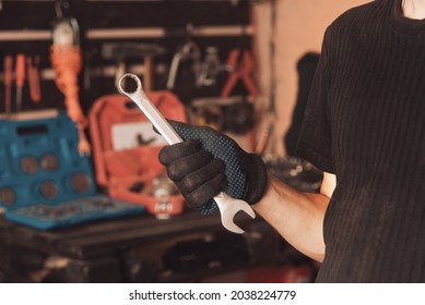 The car mechanic holds in his hand a wrench and passages on the background of a board with tools for repairing the car. Close up. Car repair garage
