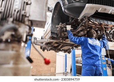 Car mechanic inspecting car steering rod and repair suspension detail. Lifted automobile at repair service station. replacement of ferrule and leverage
