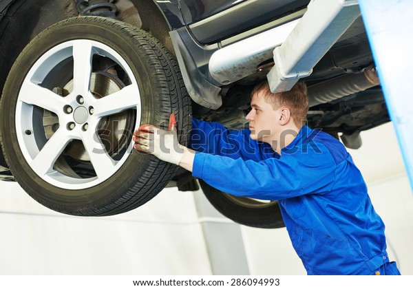 car mechanic\
inspecting suspension or brakes in car wheel of lifted automobile\
at repair service station