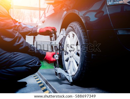 Car mechanic installing sensor during suspension adjustment. Wheel alignment work at repair service station