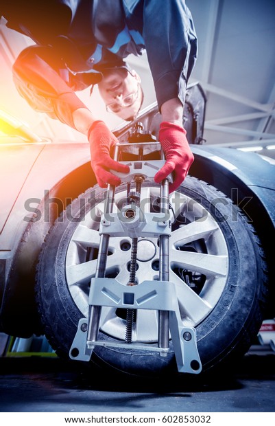 Car mechanic\
installing sensor during suspension adjustment. Wheel alignment\
work at repair service\
station