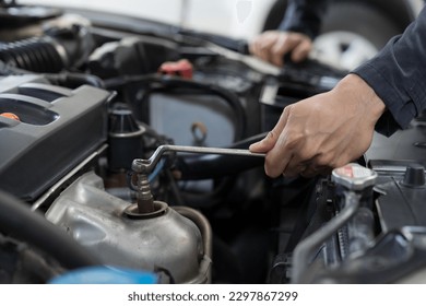 Car mechanic maintenance and auto service shop concept. Male car mechanic repair, fix car engine in auto repair shop. Technician inspecting quality parts of battery, electronic in garage workshop