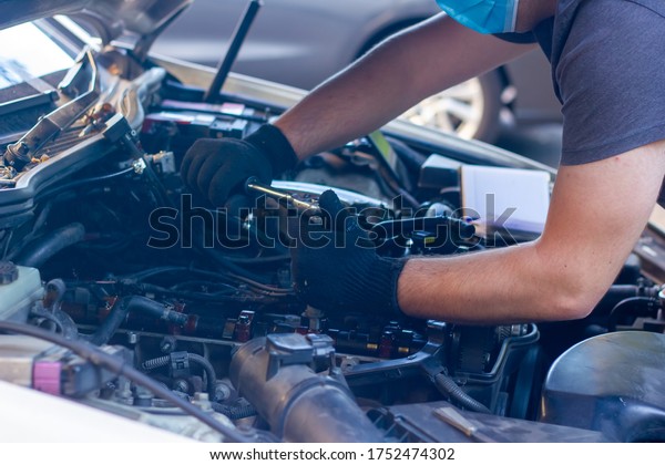 car mechanic on protective mask\
fixing car engine, auto mechanic is repairing car\
engine
