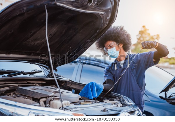 Car mechanic open car\
hood repairs system checking oil motor level for refill and clean\
in car garage service .he wearing face mask to protect from virus\
and pollution.
