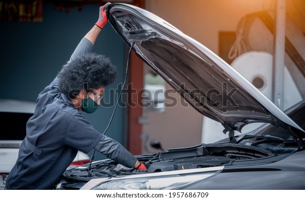 Car mechanic open car hood\
repairs and check problem system to maintenance and fixed in garage\
.he wearing face mask to protect for virus and\
pollution.