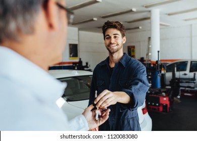 Car mechanic passing car keys to the car owner after repairing his vehicle. Mechanic giving car key to customer after servicing at garage. - Powered by Shutterstock