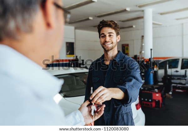 Car mechanic passing car keys to the car owner\
after repairing his vehicle. Mechanic giving car key to customer\
after servicing at garage.