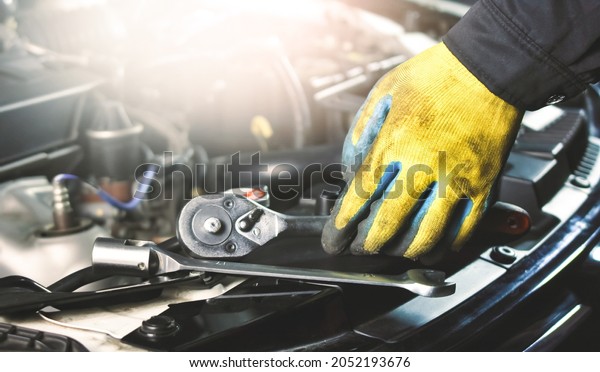 Car mechanic picking up socket wrench and\
tools on the car body in the repair\
garage