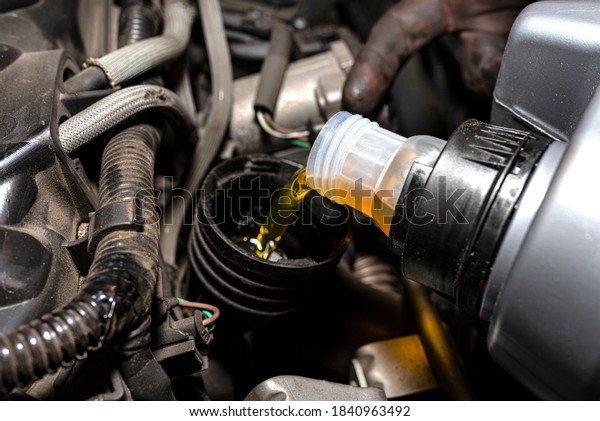 Car mechanic pours new car oil into the\
engine from a plastic tank in a car\
workshop.