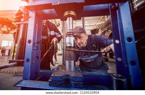 Car mechanic press new silentblock at\
repair service station. Auto service.\
Background