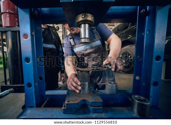 Car mechanic press new silentblock at\
repair service station. Auto service.\
Background