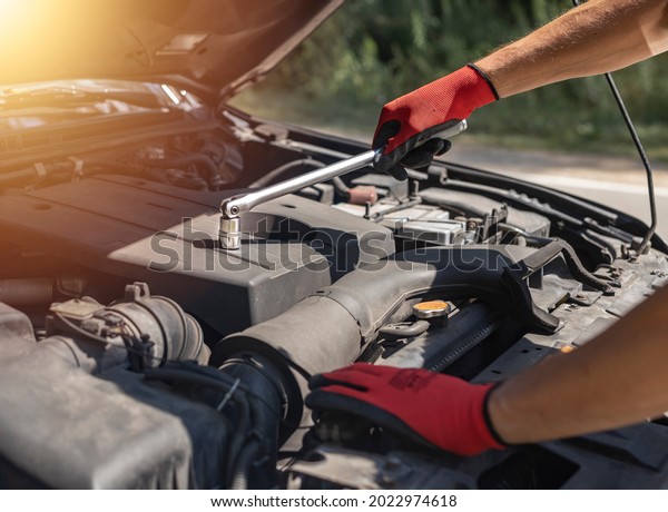 Car mechanic repairing auto engine with wrench and\
hood up on road.