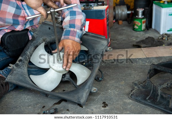 Car\
mechanic repairing cooling fan of car. Broken cooling fan motor of\
car is being removed in garage. Auto repair service.\
