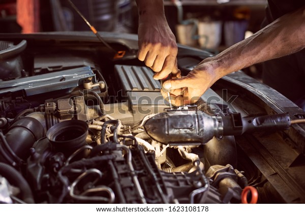 Car mechanic repairing diesel engine with\
screwdriver and flashlight helping in garage workshop. Close up\
view of old dirty auto engine and cropped car mechanic skilful\
hands. Car repairing\
concept