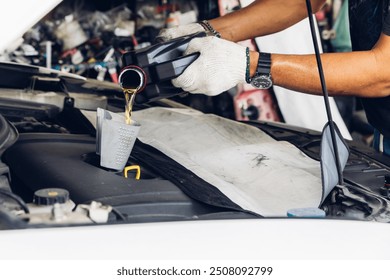 Car mechanic replacing and pouring fresh oil into engine at maintenance repair service station, Mechanic pouring oil into car at the repair garage. Fresh oil being poured during an oil change to a car - Powered by Shutterstock