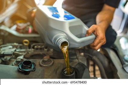 Car mechanic replacing and pouring fresh oil into engine at maintenance repair service station.