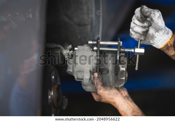 Car mechanic retracting brake pistons on a front\
brake caliper.