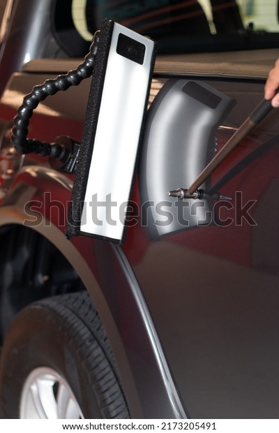 Car mechanic in car service with tools\
for repairing dents in car body without\
painting.
