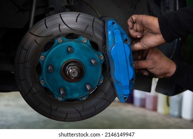 Car mechanic or serviceman disassembly and checking a disc brake and asbestos brake pads for fix and repair problem at car garage or repair shop - Shutterstock ID 2146149947