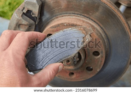 car mechanic shows a worn brake pad, a worn brake shoe and a against the background of an automobile brake disc with signs of corrosion