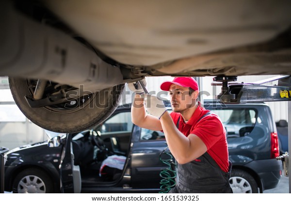 car mechanic with spanner\
tighten car suspension detail of lifted automobile at repair\
station