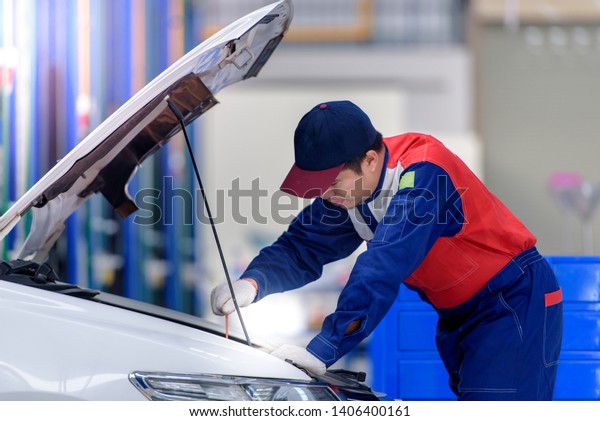 The car mechanic staff is pulling the oil level\
gauge up to check the oil level. To check the car condition., Auto\
mechanic working in garage