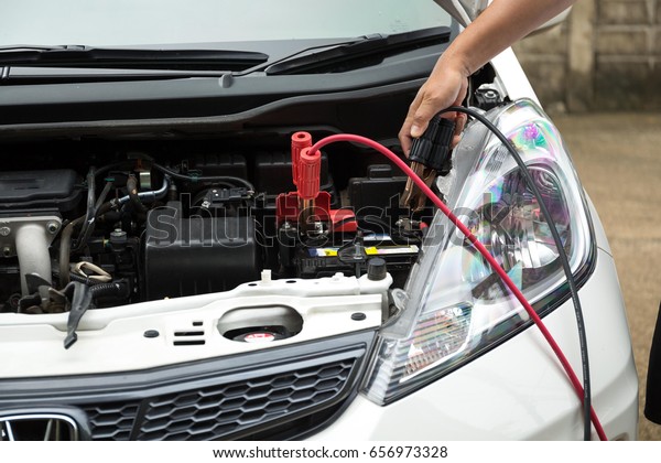 A car mechanic take off  battery jumper \
black cables after charge a dead battery\
\
