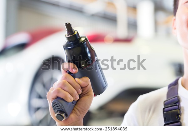car mechanic with tool in front of luxury car in\
auto workshop