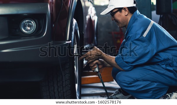 car mechanic\
in uniform at garage and service station checking and having wheels\
and tires maintenance\
service