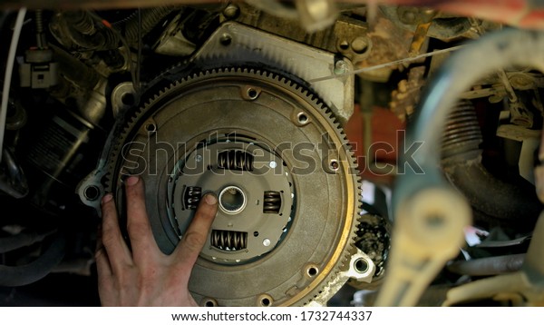 Car\
mechanic is unscrewing clutch. Car service worker with diry hands\
using electrical screwdriver to unscrew car\
clutch.