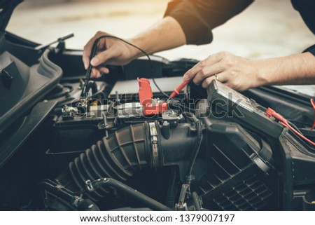 Car mechanic is using the car battery meter to measure various values and analyze it.