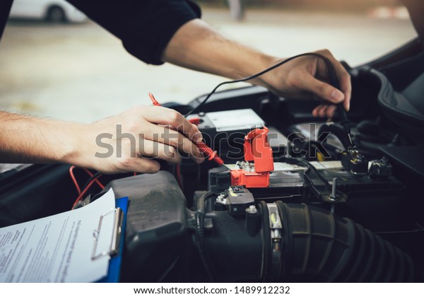 Car mechanic is using the car battery\
meter to measure various values and analyze\
it.