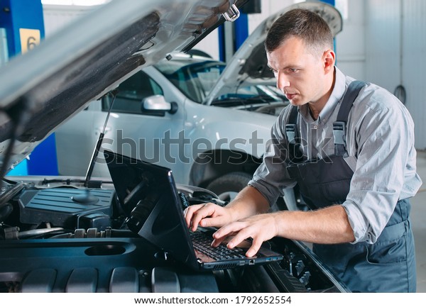 car mechanic\
using a computer laptop to diagnosing and checking up on car\
engines parts for fixing and\
repair